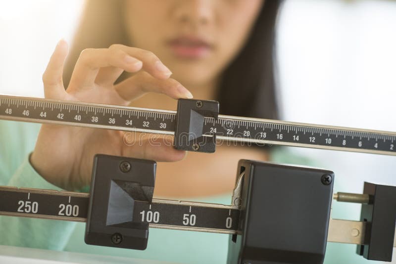 Midsection of mid adult Asian woman adjusting balance weight scale. Midsection of mid adult Asian woman adjusting balance weight scale