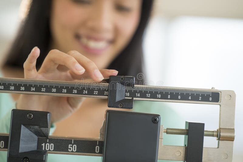 Midsection of mid adult Asian woman smiling while adjusting balance weight scale. Midsection of mid adult Asian woman smiling while adjusting balance weight scale