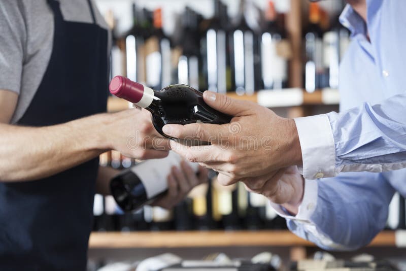 Midsection of male customer and salesman with wine bottles in shop. Midsection of male customer and salesman with wine bottles in shop