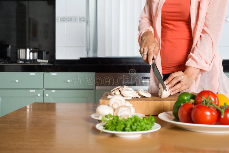 Midsection of young woman cutting vegetables on wooden chopping board at kitchen counter. Midsection of young woman cutting vegetables on wooden chopping board at kitchen counter