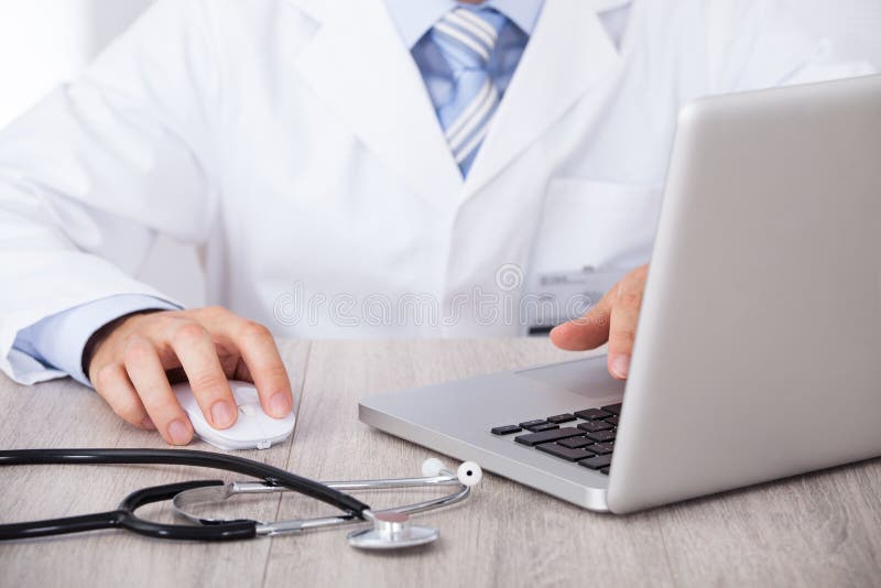 Midsection of male doctor using laptop and mouse at desk in clinic. Midsection of male doctor using laptop and mouse at desk in clinic