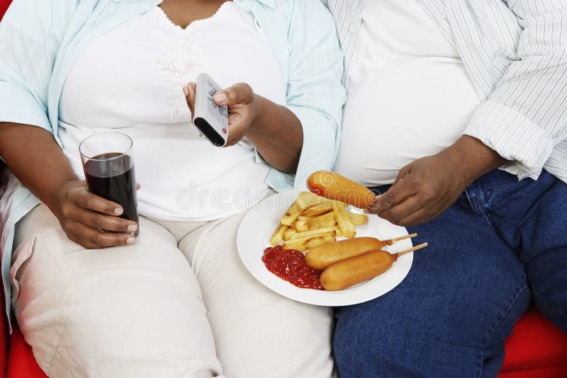 Closeup midsection of an overweight couple with junk food holding remote control. Closeup midsection of an overweight couple with junk food holding remote control