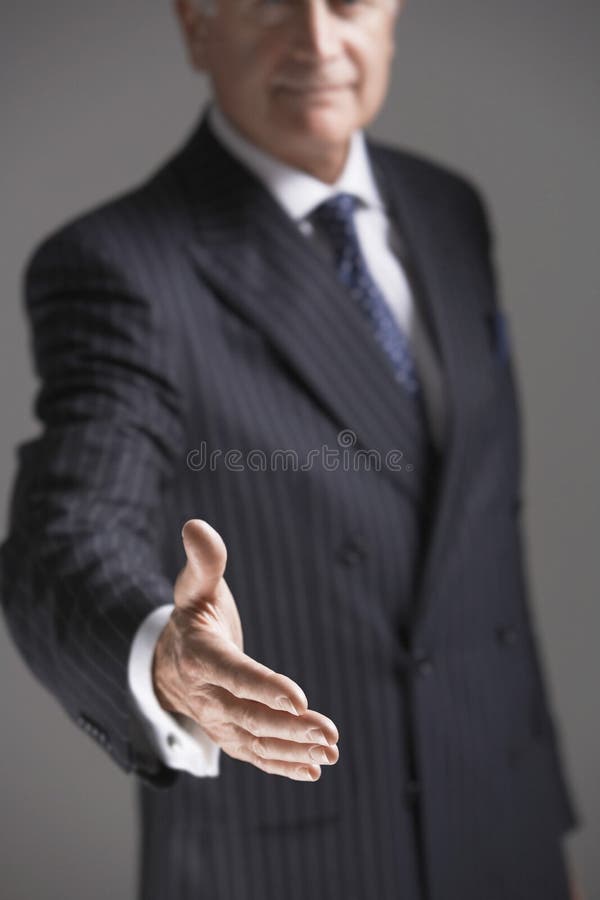 Midsection of senior businessman offering hand against gray background. Midsection of senior businessman offering hand against gray background