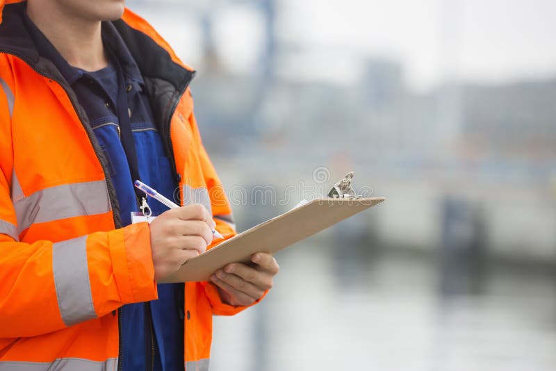 Midsection of mid adult men writing on clipboard in shipping yard. Midsection of mid adult men writing on clipboard in shipping yard