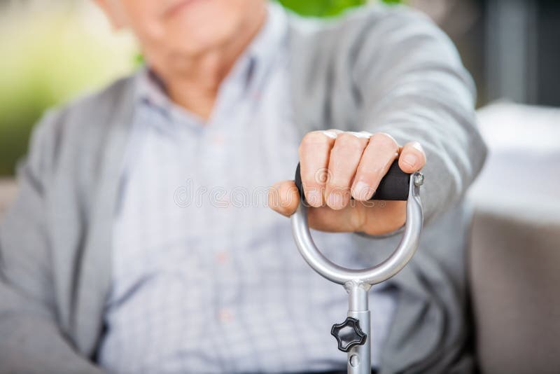 Midsection of senior man holding walking stick at nursing home. Midsection of senior man holding walking stick at nursing home