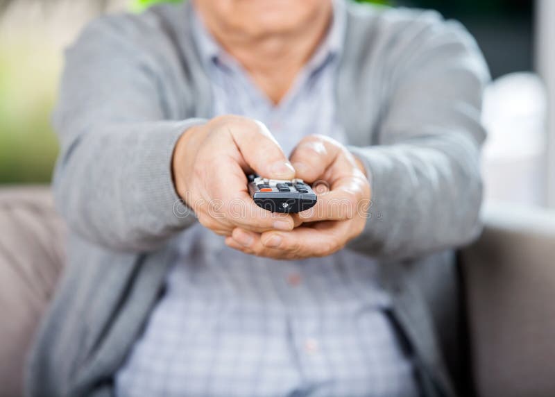 Midsection of senior man using TV remote control while sitting on couch in nursing home. Midsection of senior man using TV remote control while sitting on couch in nursing home