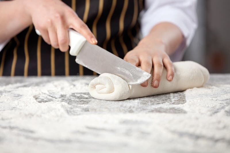 Midsection of female chef cutting rolled dough at messy counter in commercial kitchen. Midsection of female chef cutting rolled dough at messy counter in commercial kitchen