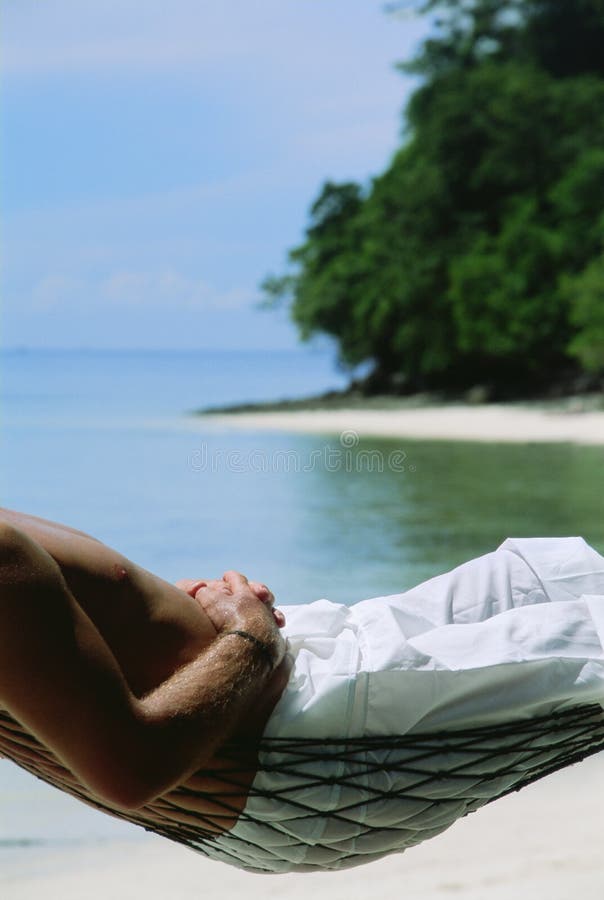 Midsection of man lying in hammock at beach. Midsection of man lying in hammock at beach.