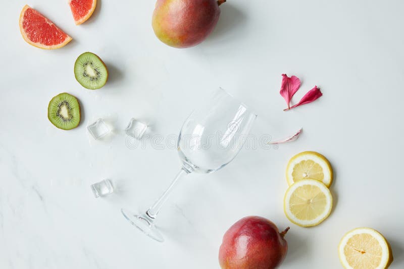 Mieszkanie kłaść z pustym wineglass, kwiatów płatkami, kostkami lodu i asortowanymi egzotycznymi owoc na białym tabletop fotografia stock