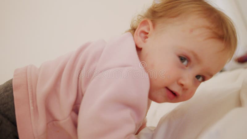 Mignon bébé assis sur un lit qui joue du roulement et rire banque de vidéos