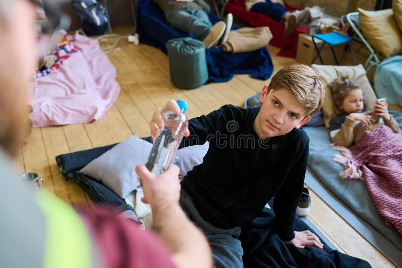 Mignon garçon de préadolescents en vêtements de banal prenant une bouteille d'eau lui a passé par volontaire images stock