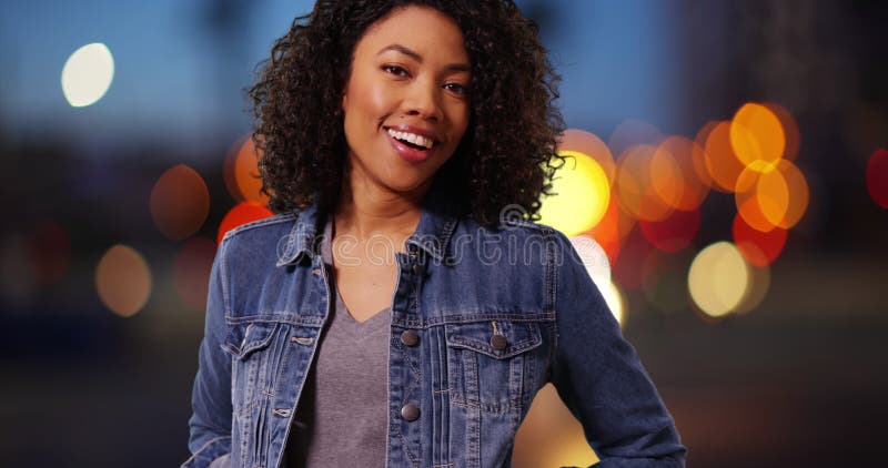 Mignonne femme africaine souriant devant la caméra en milieu urbain avec lumières bokeh banque de vidéos
