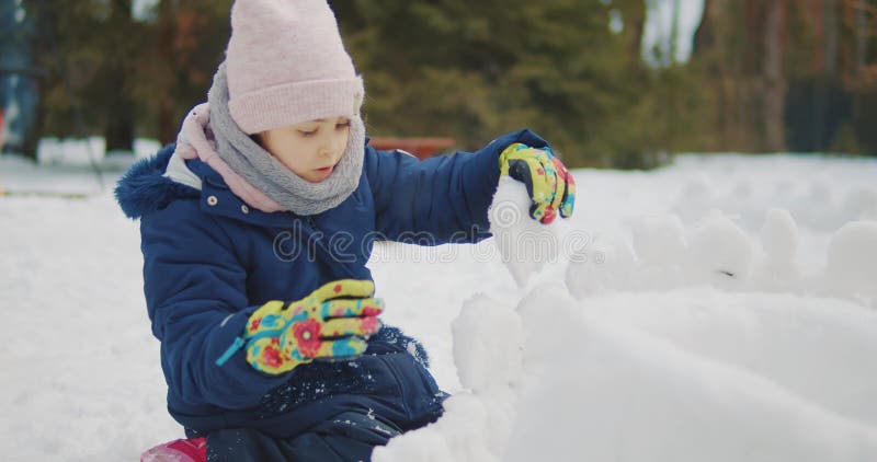 Mignonne fille construit et joue dans la neige dans la forêt