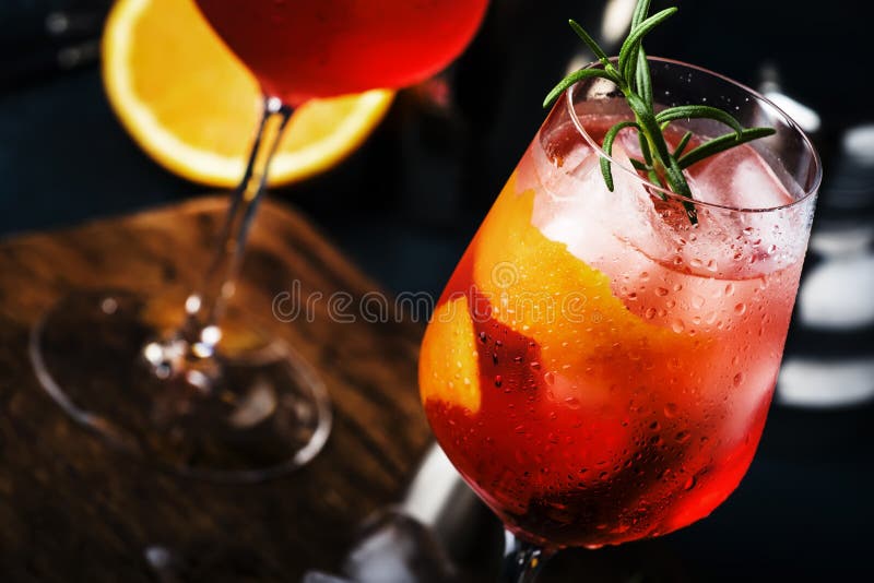 Milano spritzer alcoholic cocktail with red bitter, dry white wine, soda, zest and ice. Dark blue background, bar tools, selective