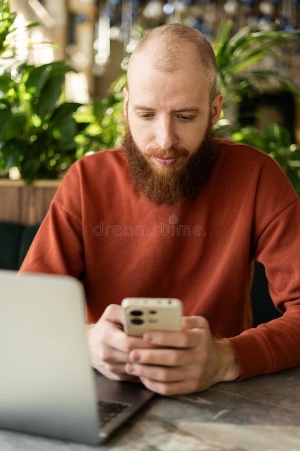 Milenés usando celulares para charlar mientras se sienta cerca de una laptop en la oficina fotografía de archivo