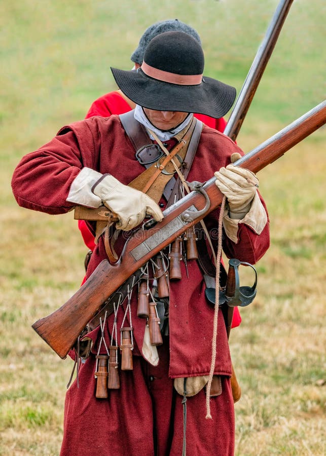 Reenactors dressed as English Civil War militia priming their matchlock muskets. These civilians defended the City of Worcester during the 1642–1651 civil war. The militiaman in the foreground holds a Matchlock musket and match cord or slow match in one hand. In the other hand he is holding a priming flask. Both musketeers wear bandoliers from which hang the musket blackpowder charges. Part at the M5 Living History Show at Spetchley Park in Worcestershire. Reenactors dressed as English Civil War militia priming their matchlock muskets. These civilians defended the City of Worcester during the 1642–1651 civil war. The militiaman in the foreground holds a Matchlock musket and match cord or slow match in one hand. In the other hand he is holding a priming flask. Both musketeers wear bandoliers from which hang the musket blackpowder charges. Part at the M5 Living History Show at Spetchley Park in Worcestershire.