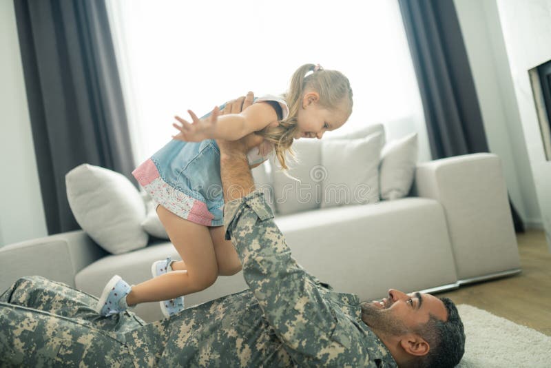 Militar que miente en el piso y que levanta a su hija preciosa linda fotos de archivo Militar que miente en el piso y que levanta a su hija preciosa linda fotos de archivo