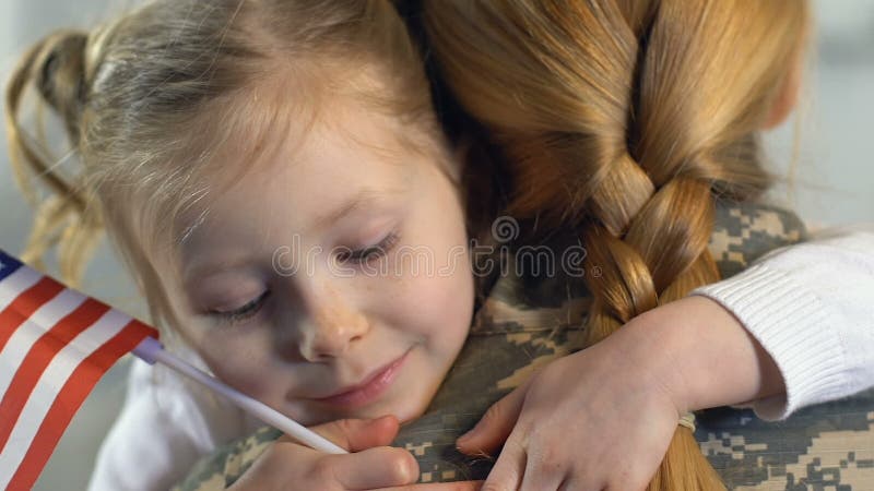 Military woman hugging daughter holding national flag, independence day, patriot