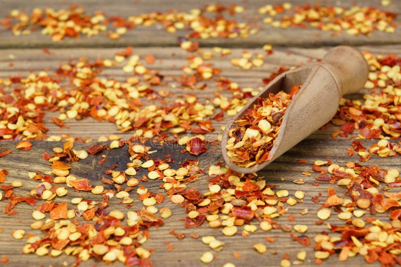 Milled Chili Peppers Flakes And Corns On Wooden Board
