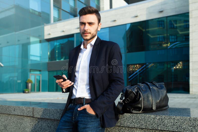Millennial affärsman med en mobiltelefon i hans händer Stilfull man för ung lyckad affär med en svartläderpåse fotografering för bildbyråer Millennial affärsman med en mobiltelefon i hans händer Stilfull man för ung lyckad affär med en svartläderpåse fotografering för bildbyråer