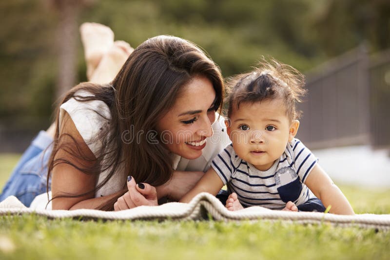 Millennial Hispanic mother lying on a blanket in the park with her baby smiling, close up stock photography Millennial Hispanic mother lying on a blanket in the park with her baby smiling, close up stock photography