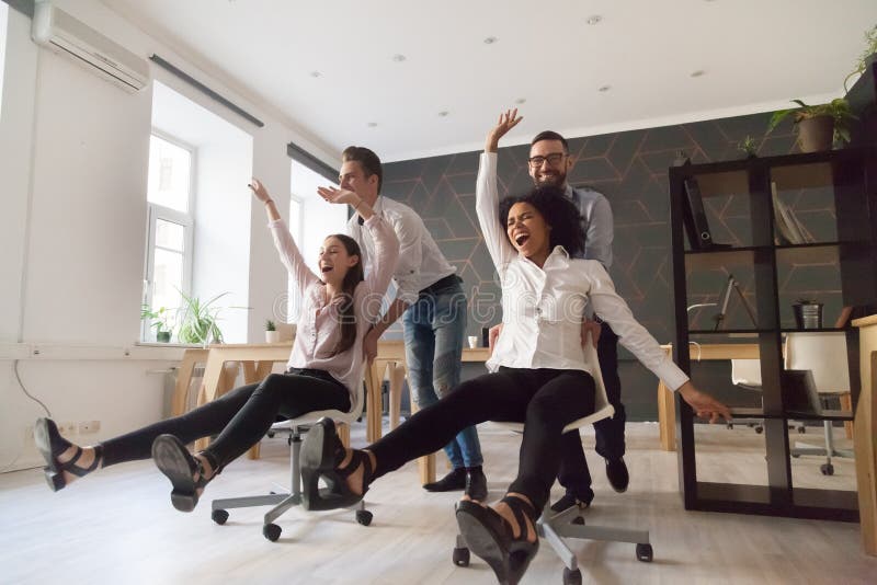 Millennial multiracial people having funny ride on chairs in off stock photo Millennial multiracial people having funny ride on chairs in off stock photo