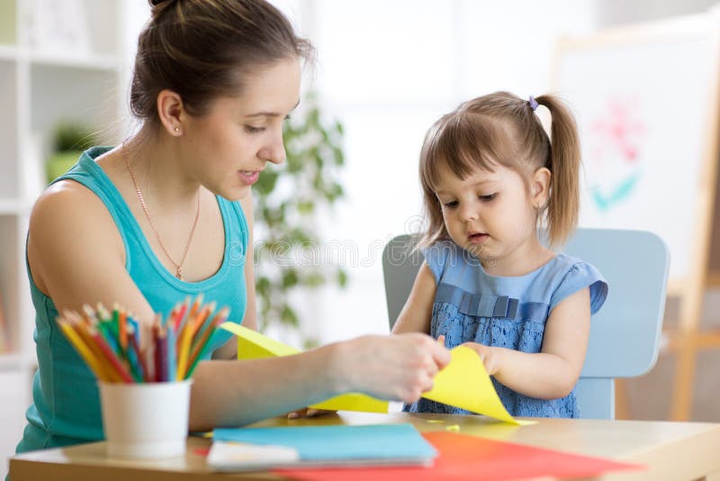Madre ayudando a su hijo/a a cortar papel de colores fotos de archivo