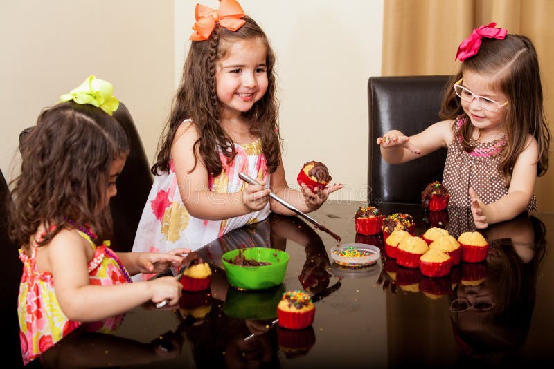 Gorgeous little cousins baking and decorating some cupcakes with chocolate and having fun at home. Gorgeous little cousins baking and decorating some cupcakes with chocolate and having fun at home