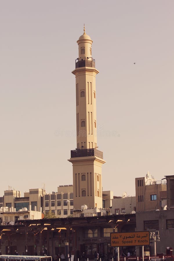 Minarets are the main architectural feature that stand out mosques. Beautiful single minaret of mosque. muslim worship. religious. peaceful view of plain sky and beige minaret of mosque. upward shot of picture. There are buildings in surroundings.