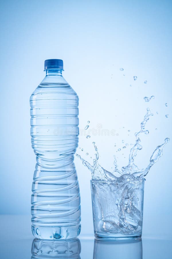 Mineral Water Bottle and Water Glass with Spash on Blue Background with Copy Space. Vertical