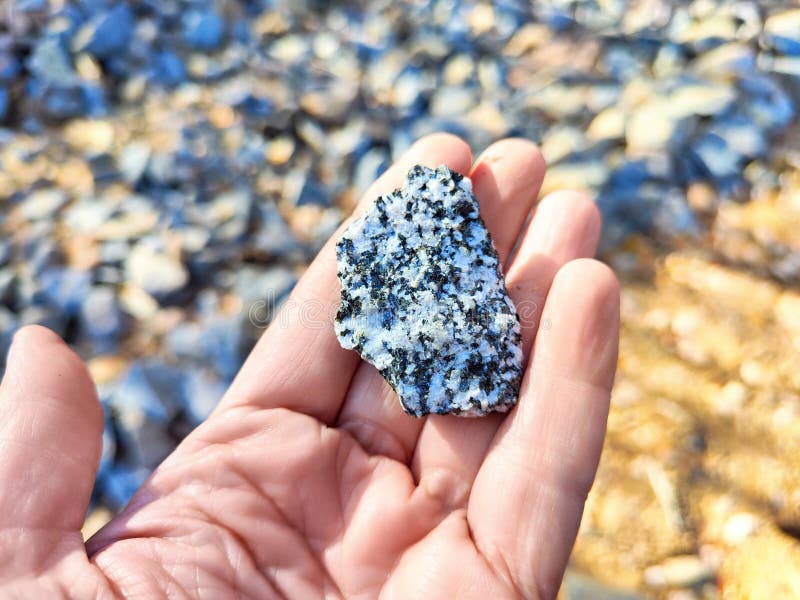 Mineralvetenskapen. en hand håller en bit granitsten mot en bakgrund av andra klippor royaltyfri foto