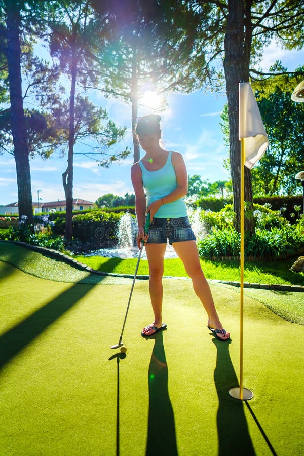 Mini Golf - Frau, die Golf auf grünem Gras bei Sonnenuntergang spielt lizenzfreies stockfoto Mini Golf - Frau, die Golf auf grünem Gras bei Sonnenuntergang spielt lizenzfreies stockfoto