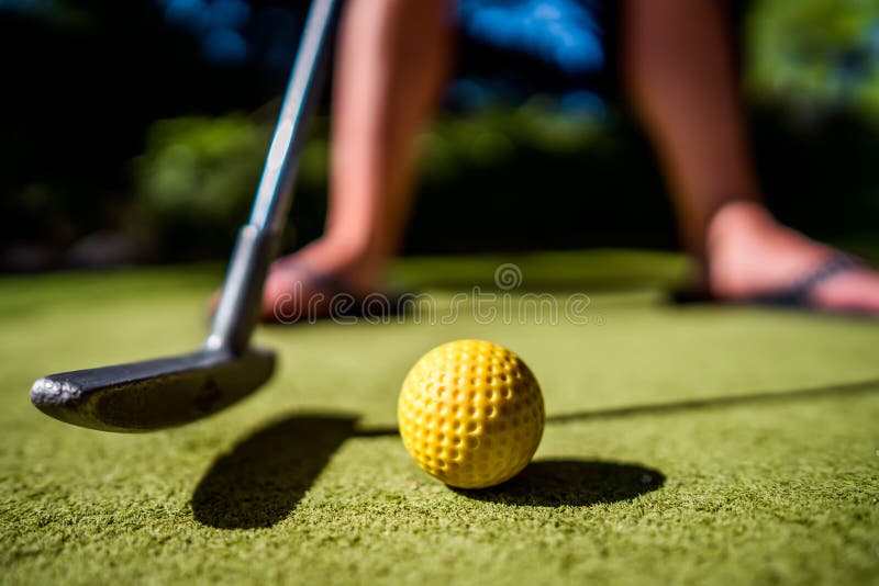 Mini Golf yellow ball with a bat near the hole at sunset