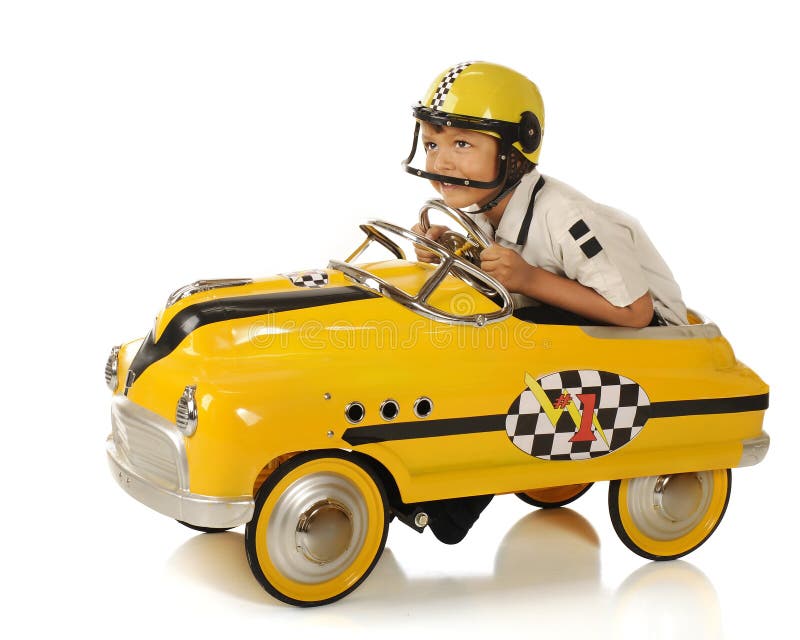 An adorable preschooler wearing a helmet with a visor, leaning forward as he races his bright yellow pedal car. Isolated. An adorable preschooler wearing a helmet with a visor, leaning forward as he races his bright yellow pedal car. Isolated.