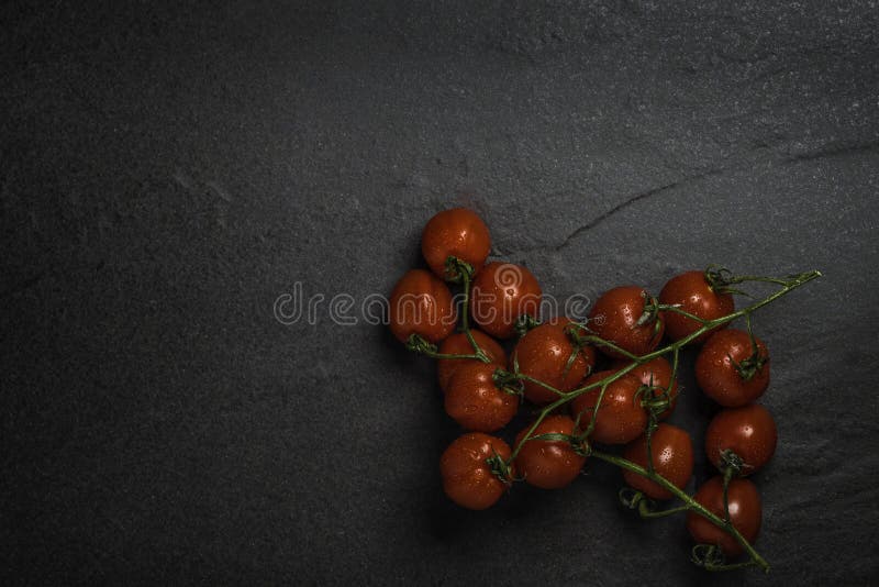 Mini tomates-cerises mûres organiques de vigne de Roma sur un fond en pierre foncé images stock Mini tomates-cerises mûres organiques de vigne de Roma sur un fond en pierre foncé images stock
