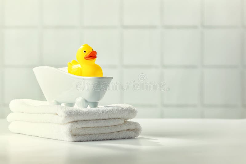 A miniature bubble bath, yellow rubber duck and white towels on bathroom countertop, children bath accessories, baby