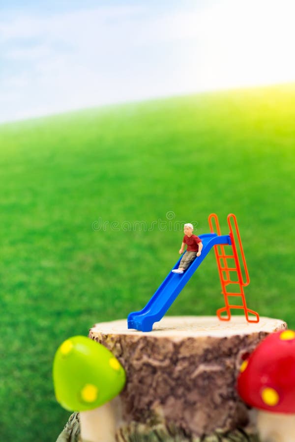 Miniature children: The boy is playing slider happily with a vast green meadow. Image use for Children`s Day.