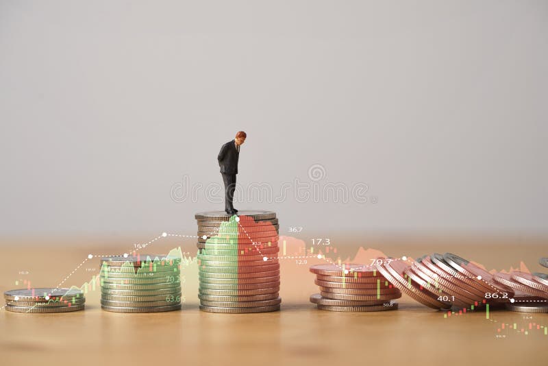 Miniature figure standing on highest coins stacking with increasing and decreasing stock market graph and chart for Business investment growth and Economic recession concept.