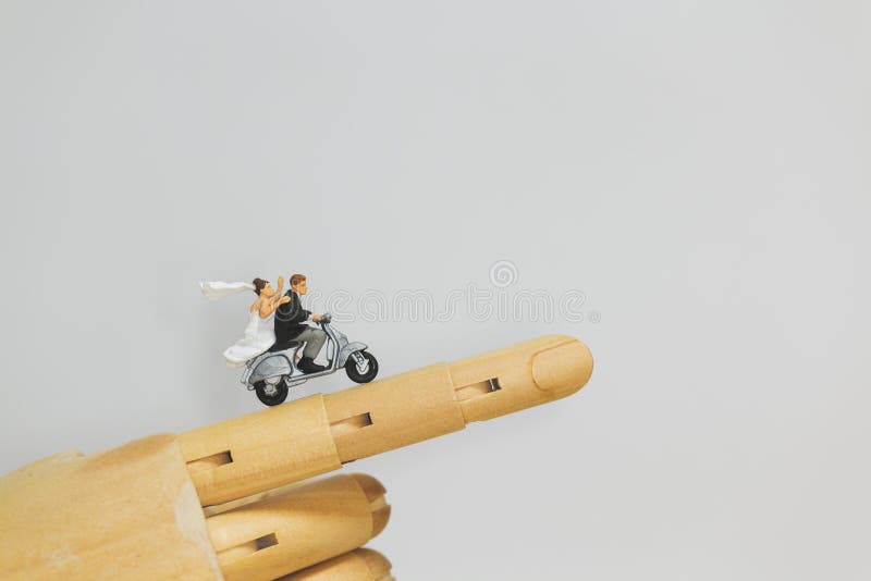 Miniature people : Couple riding the motorcycle on wooden hand with grey background
