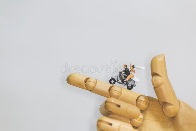 Miniature people : Couple riding the motorcycle on wooden hand with grey background