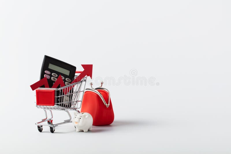 Shopping cart trolley, calculator, piggy bank, coin purse and red arrow up on white background with copy space. Crisis royalty free stock image