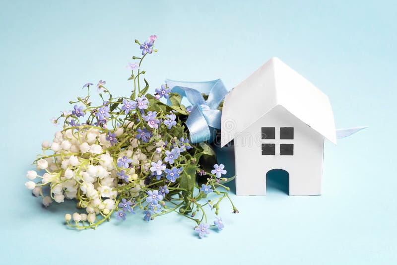 Miniature white toy house with bouquet of lily of the valley and forget-me-nots on a blue background. Miniature white toy house with bouquet of lily of the valley and forget-me-nots on a blue background