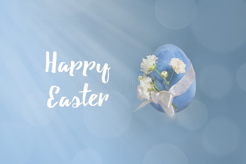 Minimal easter concept. Painted blue quail egg tied with a ribbon and a delicate white flower on a textured background with bokeh and rays. Minimal background. Modern Easter.