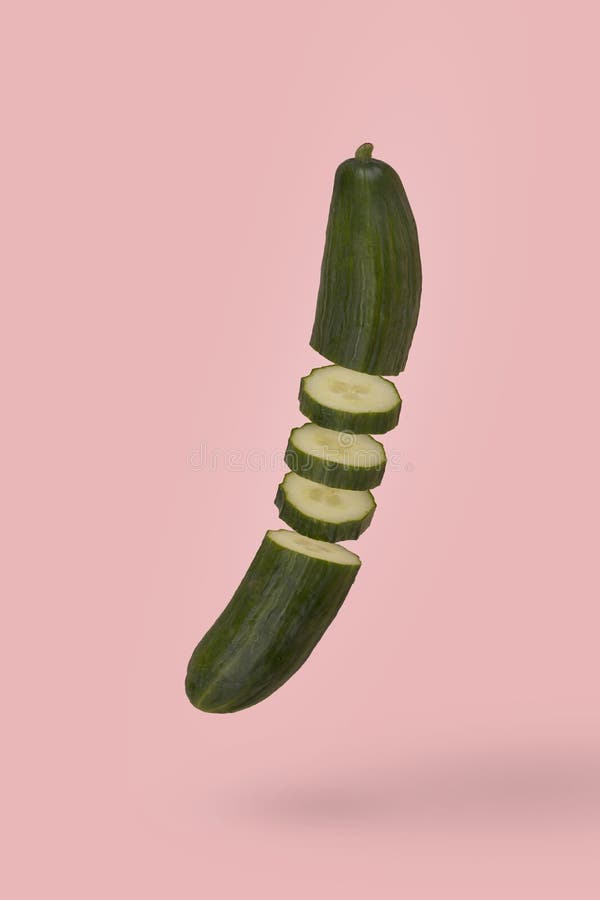 Minimal idea with fresh sliced cucumber floating in air isolated on pastel pink background. Diet, vitamins, vegan and healthy food