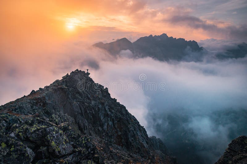 Minimalistická fotografie, turista na vrcholu kopce. Mlha v údolí hor. Podzimní příroda, západ slunce světlo v pozadí