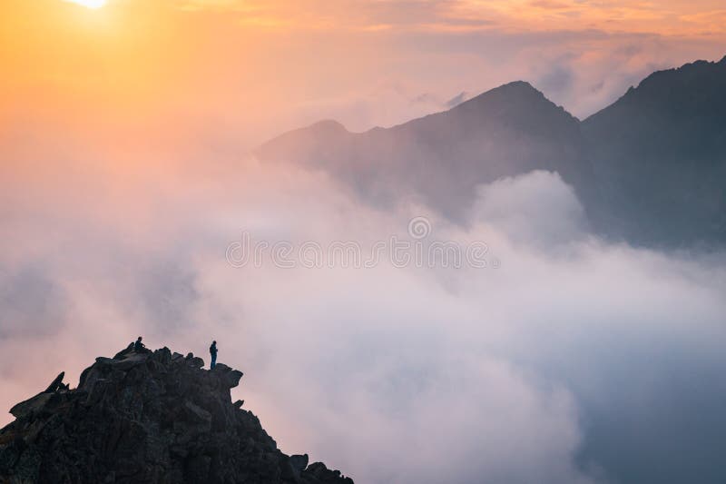 Minimalistická fotografie, turista na vrcholu kopce. Mlha v údolí hor. Podzimní příroda, západ slunce světlo v pozadí