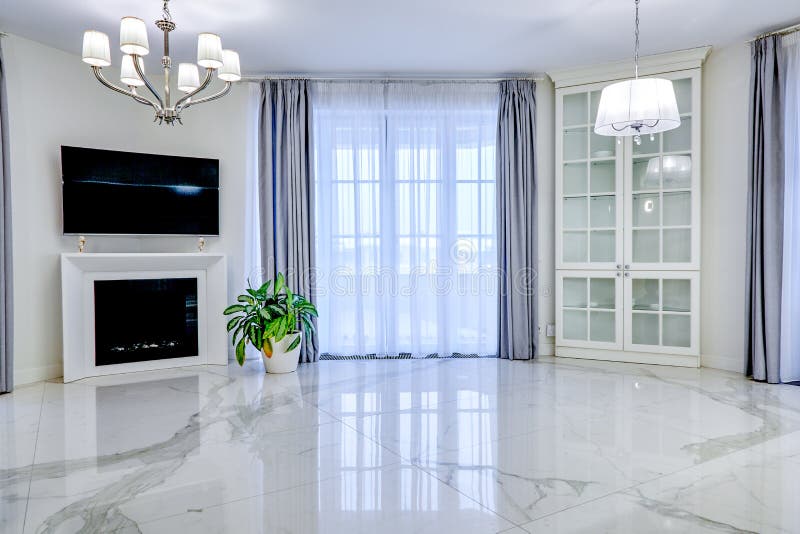 Minimalistic interior of living room in light tone with marble flooring, large windows and fireplace under TV.