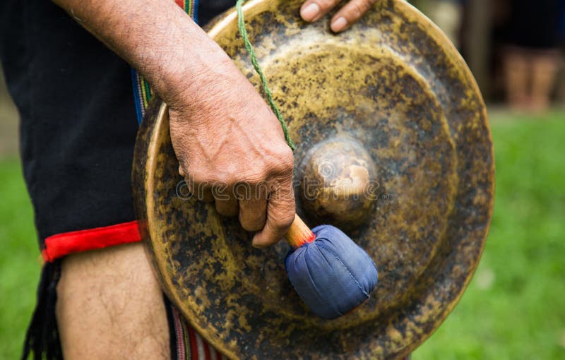 Minority man in traditional dress knocking a copper gong stock photo Minority man in traditional dress knocking a copper gong stock photo