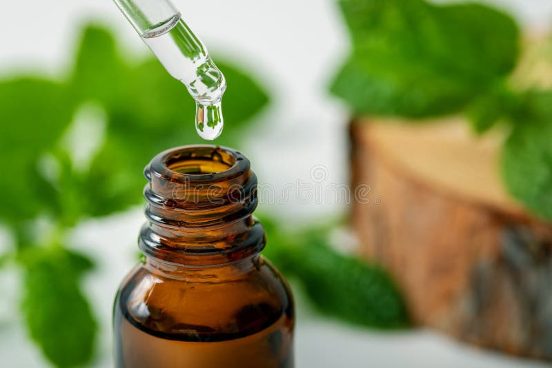 Mint essential oil drop falling from dropper into the bottle