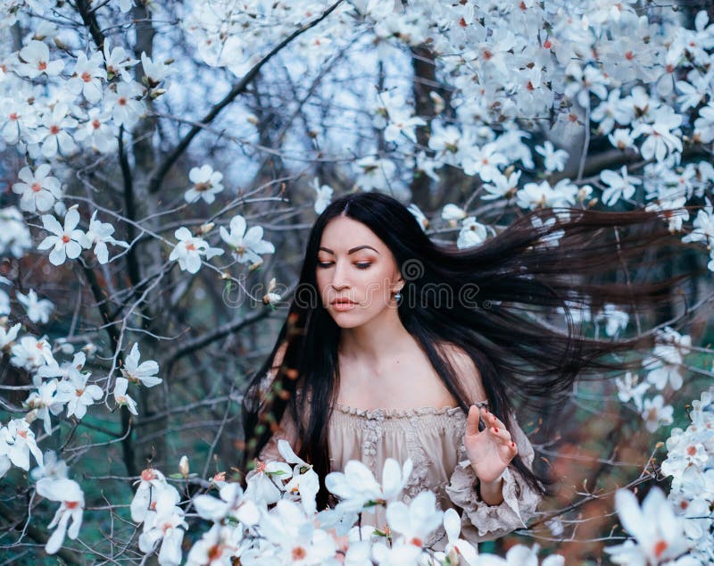 Minunată doamnă cu părul negru și frumos cu ochii închiși stă în grădina magnoliilor înfloriți. părul se ridică în sus royalty free stock image